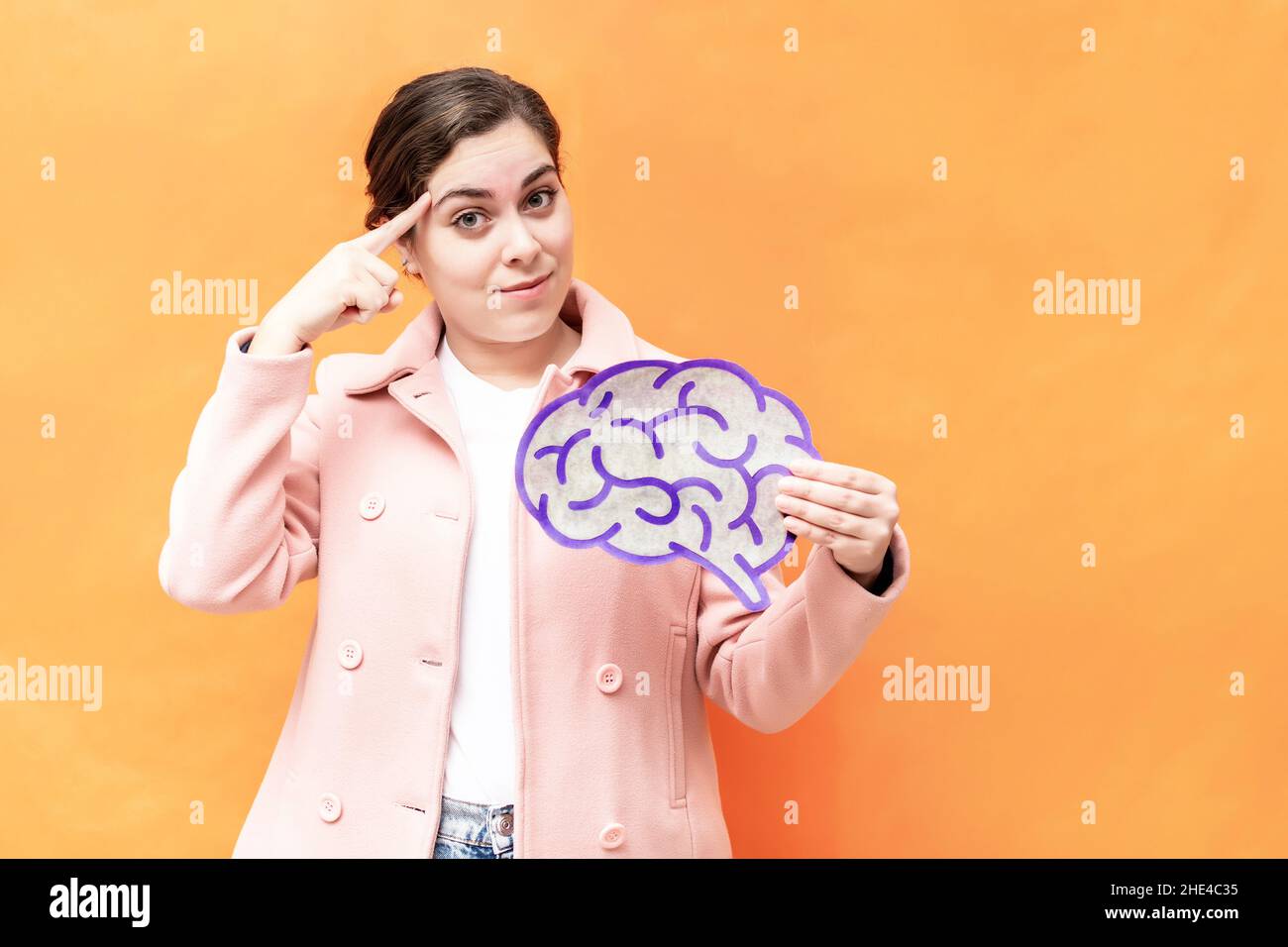 Portrait with brain figure and brainstorming concept. Businesswoman holding brain figure on orange background. Mental health protection and care. Stock Photo