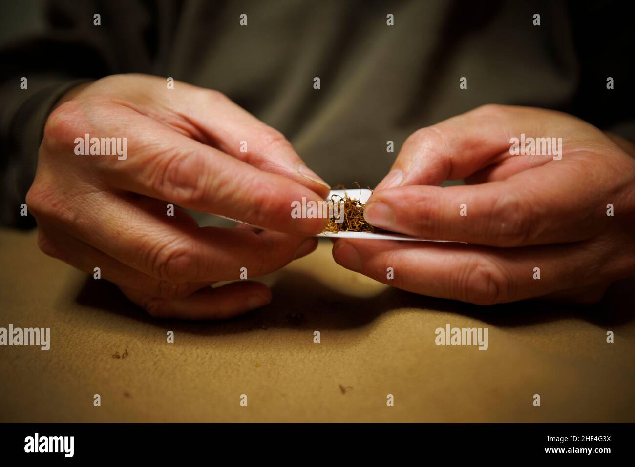 A man rolls a cigarette paper and fills it with loose tobacco Stock Photo