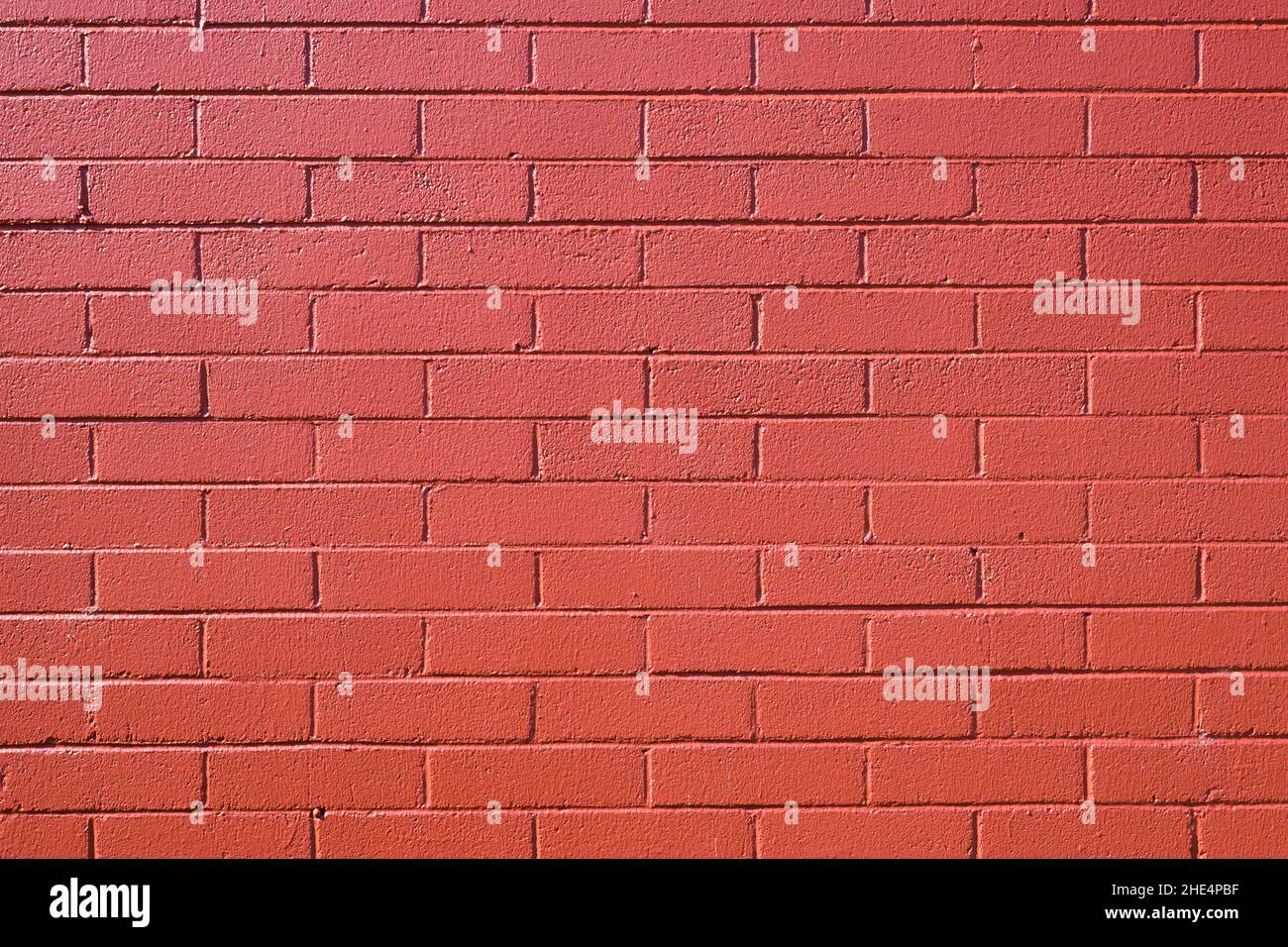 A brick wall is painted in a coat of red paint to create a pattern Stock Photo