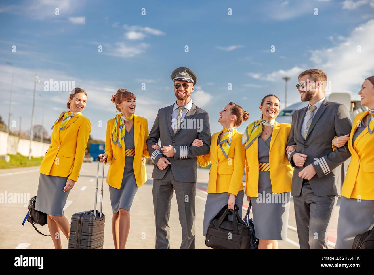 Joyful women stewardesses holding travel bags and smiling while standing at airport with male pilots Stock Photo