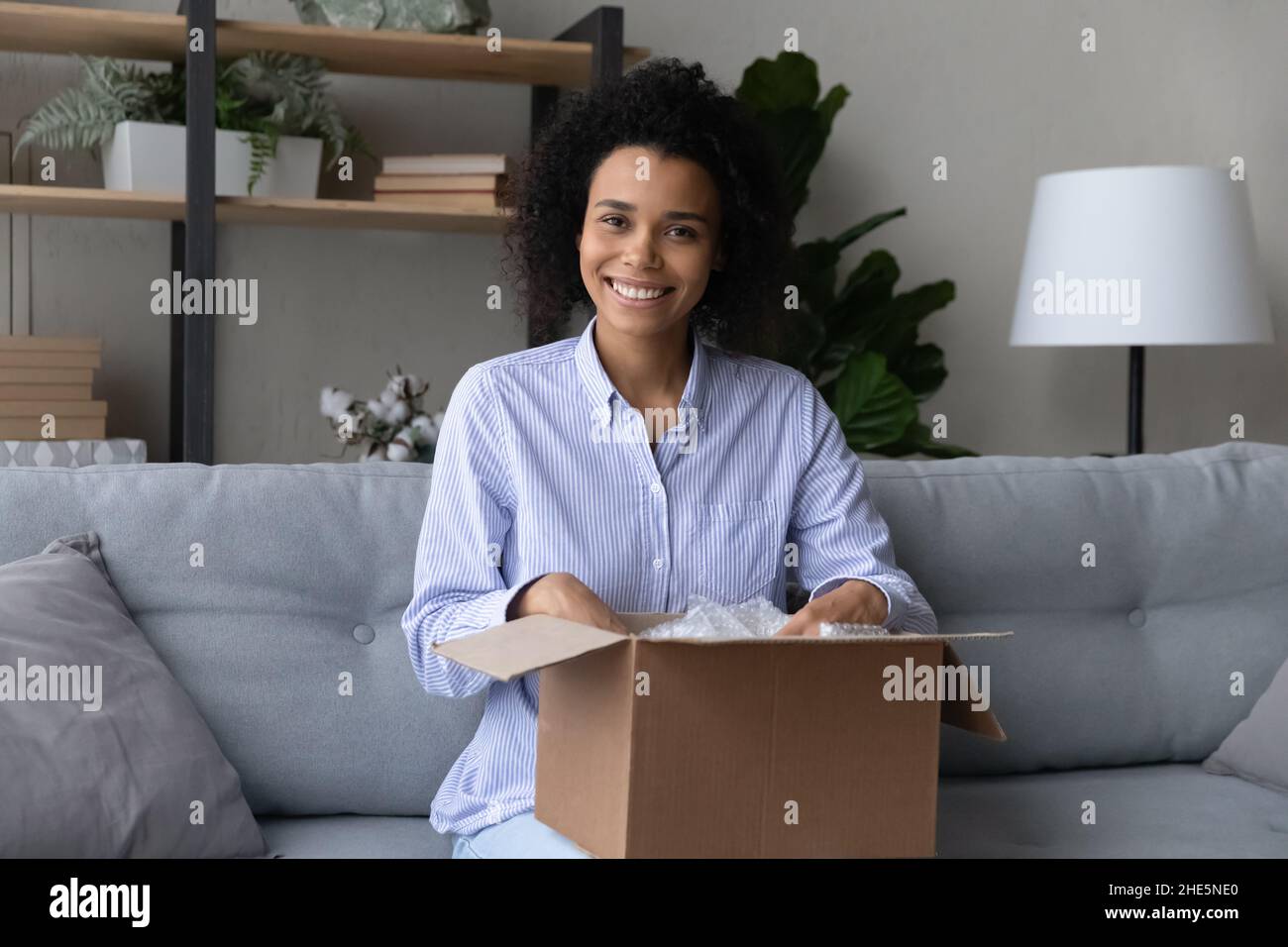 Smiling young african american woman unpacking carton box. Stock Photo