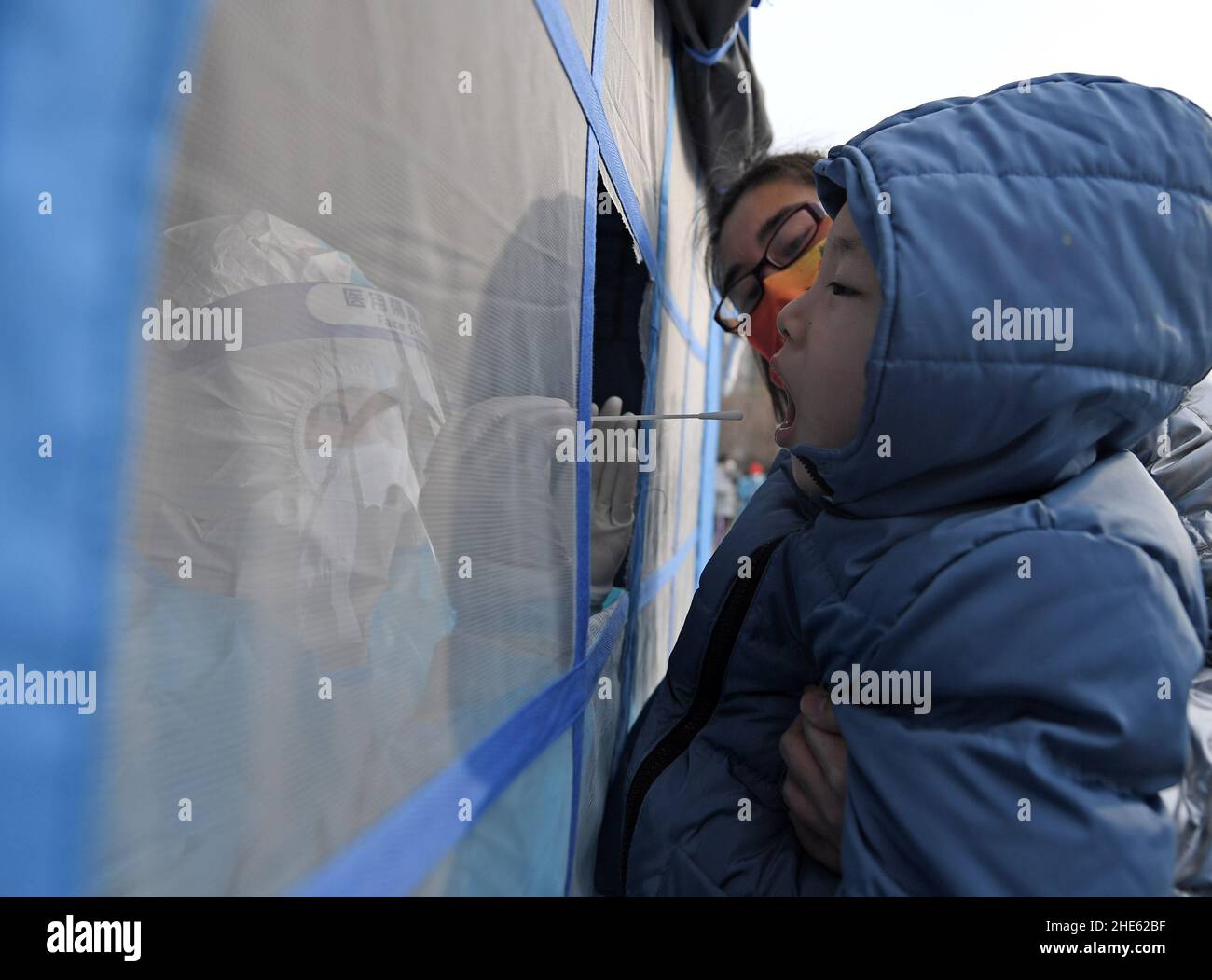 Tianjin, China. 09th Jan, 2022. A medical worker takes a swab sample from a child, accompanied by a parent, for nucleic acid test at a testing site of Binhai New Area in north China's Tianjin, Jan. 9, 2022. North China's Tianjin, a municipality that neighbors Beijing, has decided to start a citywide nucleic acid testing after 20 people tested positive for COVID-19, authorities said Sunday. The infections were reported from 6 p.m. Friday to 9 p.m. Saturday in Jinnan District, and the gene sequencing found the first two locally transmitted confirmed cases were infected with the V Credit: Xinhua/ Stock Photo