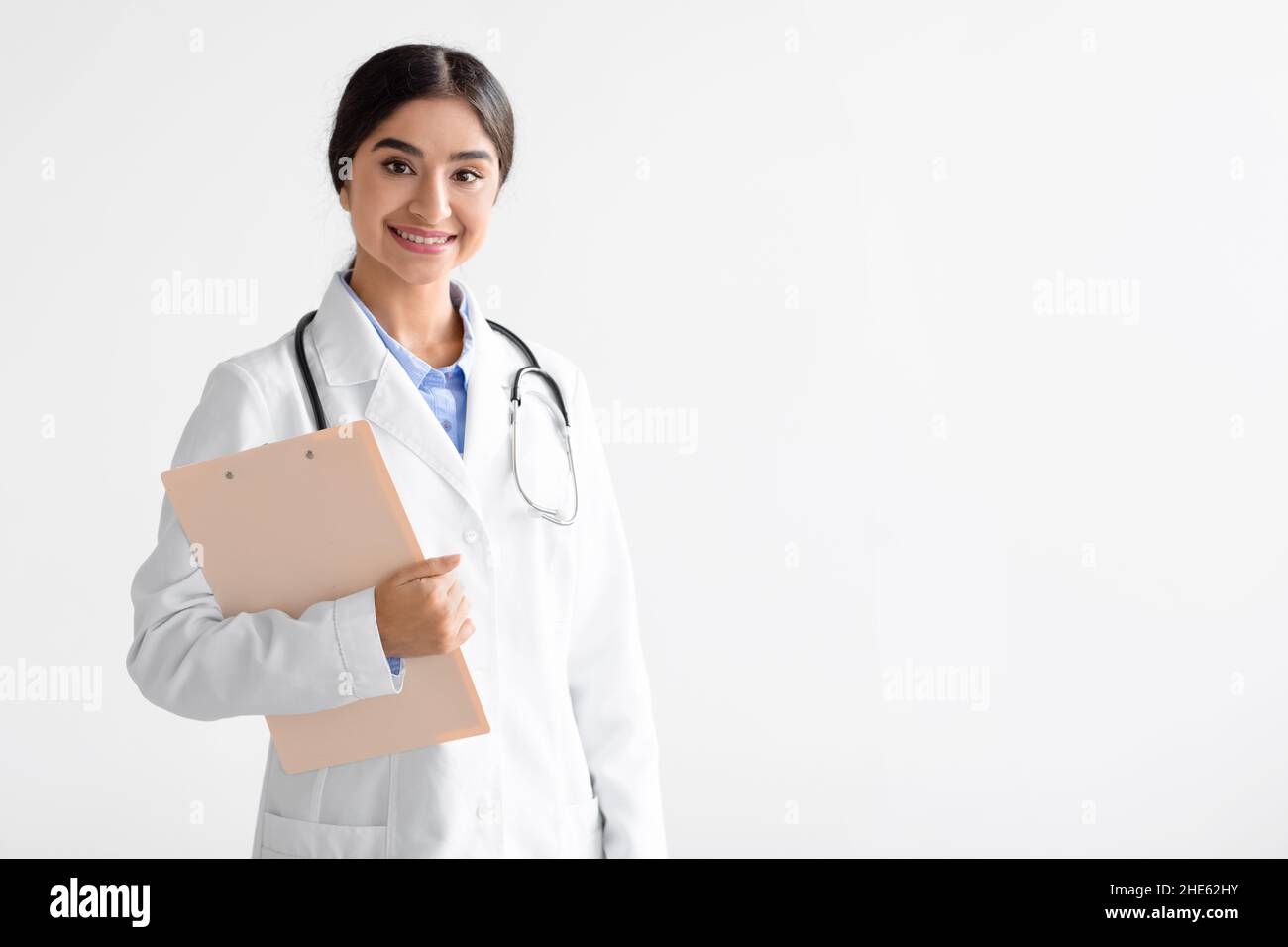 Friendly young cute indian female doctor in uniform with tablet in hands looking at camera isolated on white background Stock Photo