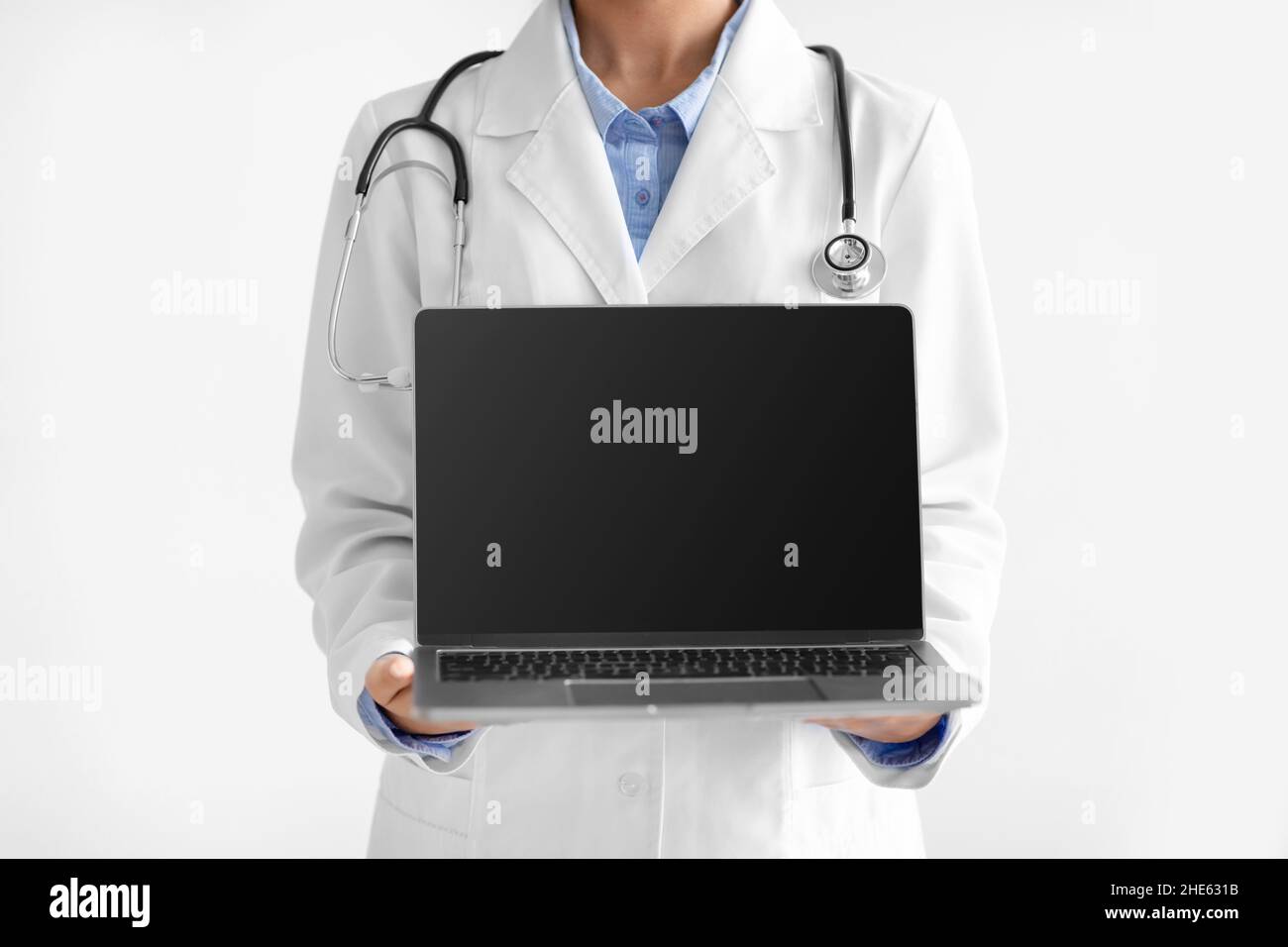 Young indian female doctor in uniform shows computer with empty screen isolated on white background, unrecognizable Stock Photo