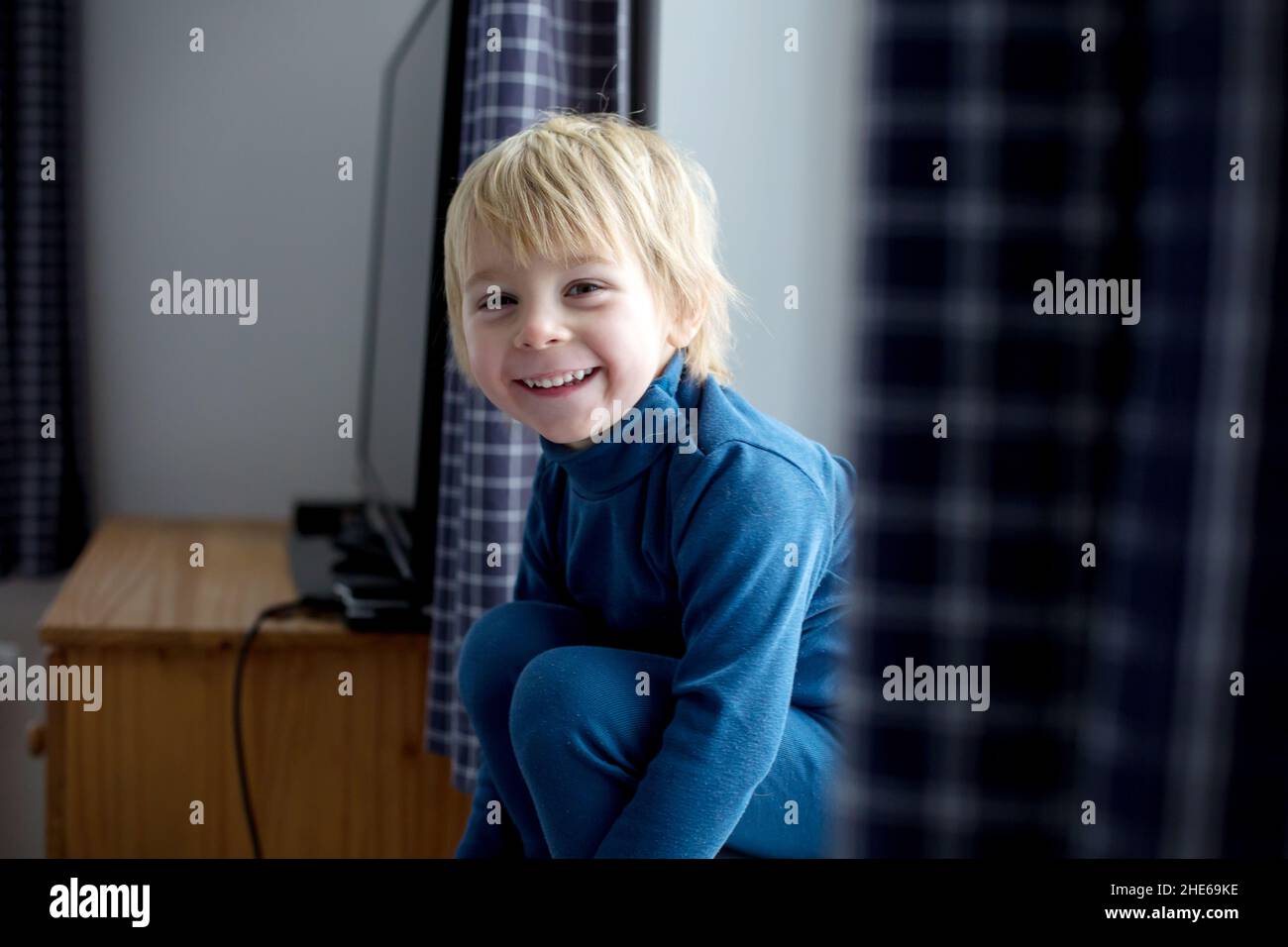 Toddler child, sitting on the window, watching the snow falling, reading little book Stock Photo