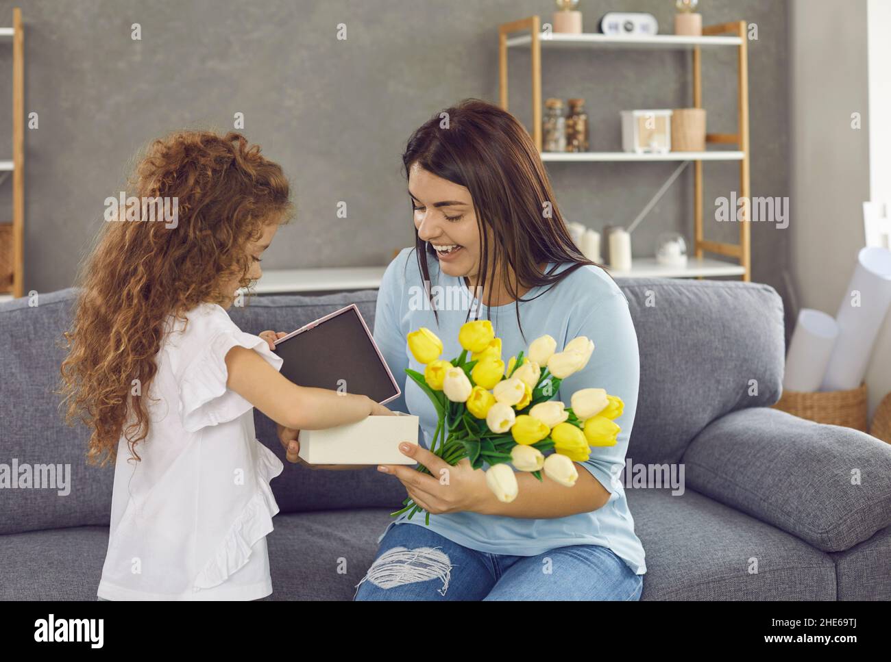 Little daughter congratulates her loving mother on holiday by giving gifts and flowers. Stock Photo