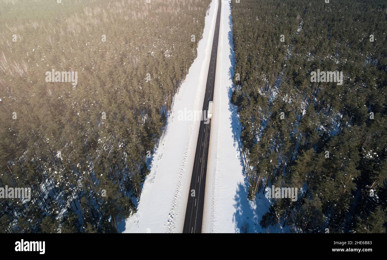 Cargo truck moving on highway road around snowy forest aerial above top view Stock Photo