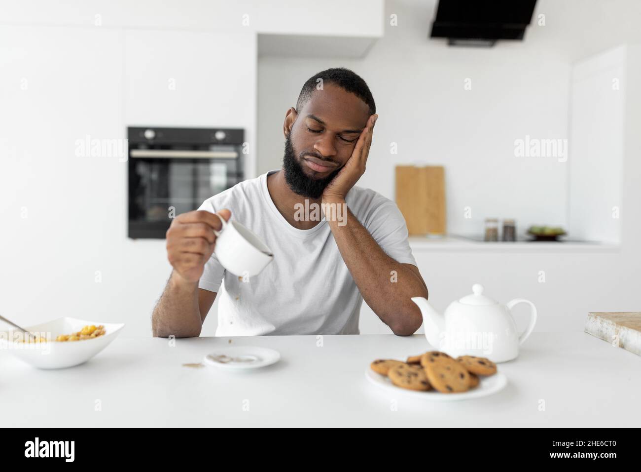 Black man yawning, pouring coffee away from cup Stock Photo