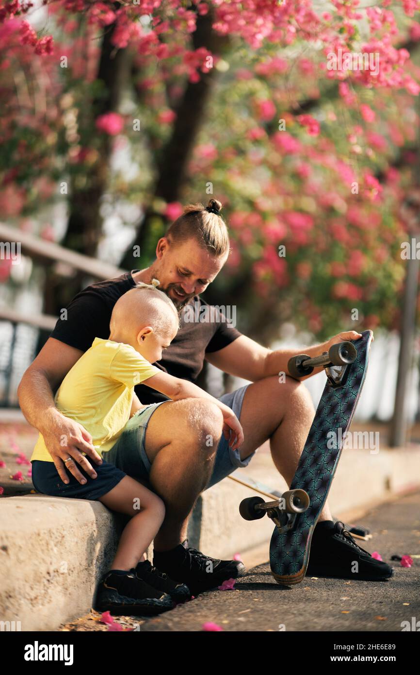 Father is hugging his little son in skate park. Springtime. Real family. Spending quality time together Stock Photo