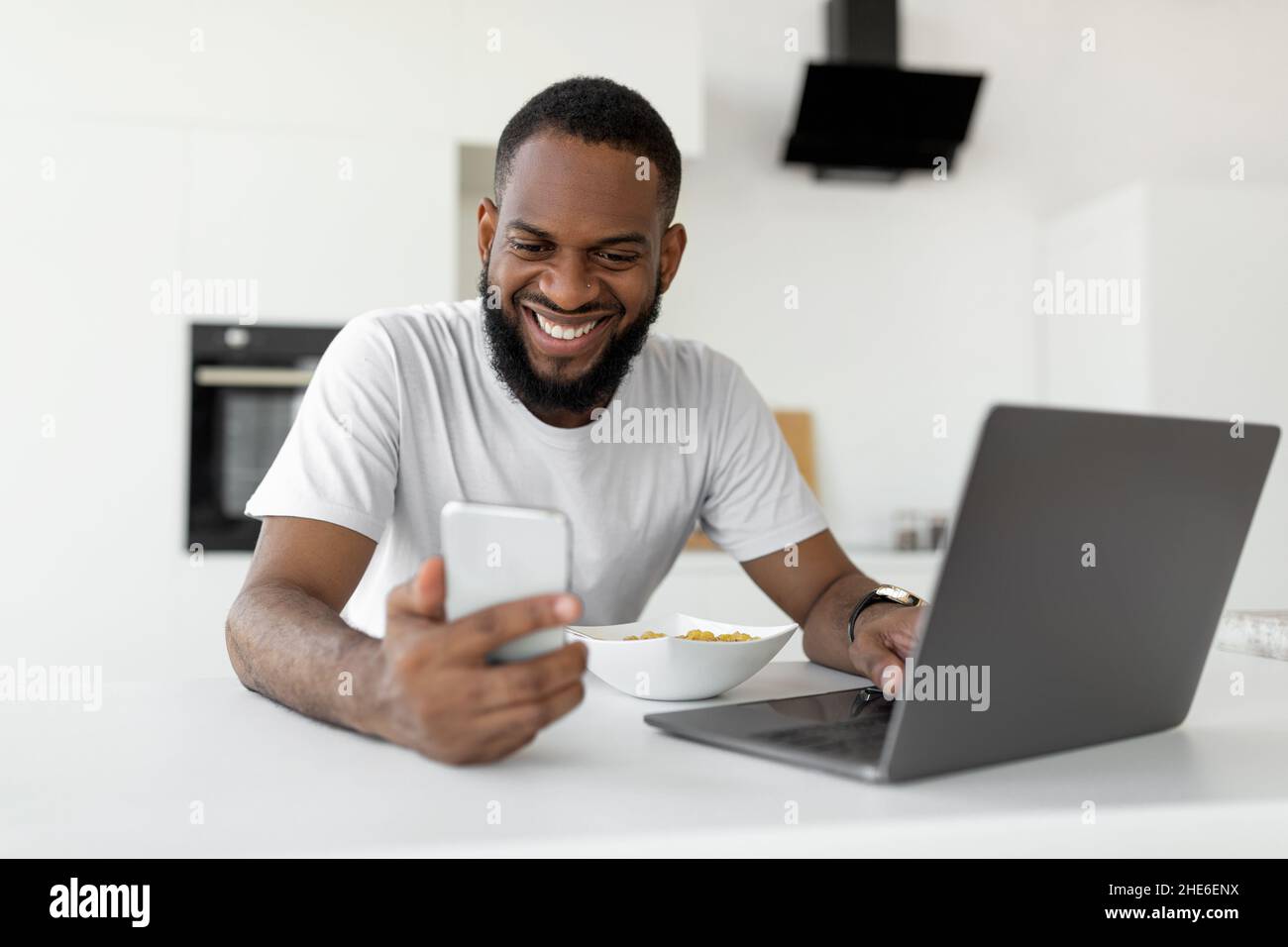 Black man using pc and smartphone having breakfast at home Stock Photo