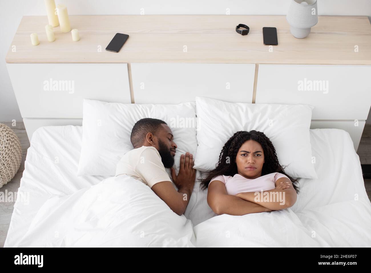 Upset young black woman lie on white bed with crossed arms on her chest think about problems, suffers from noise Stock Photo