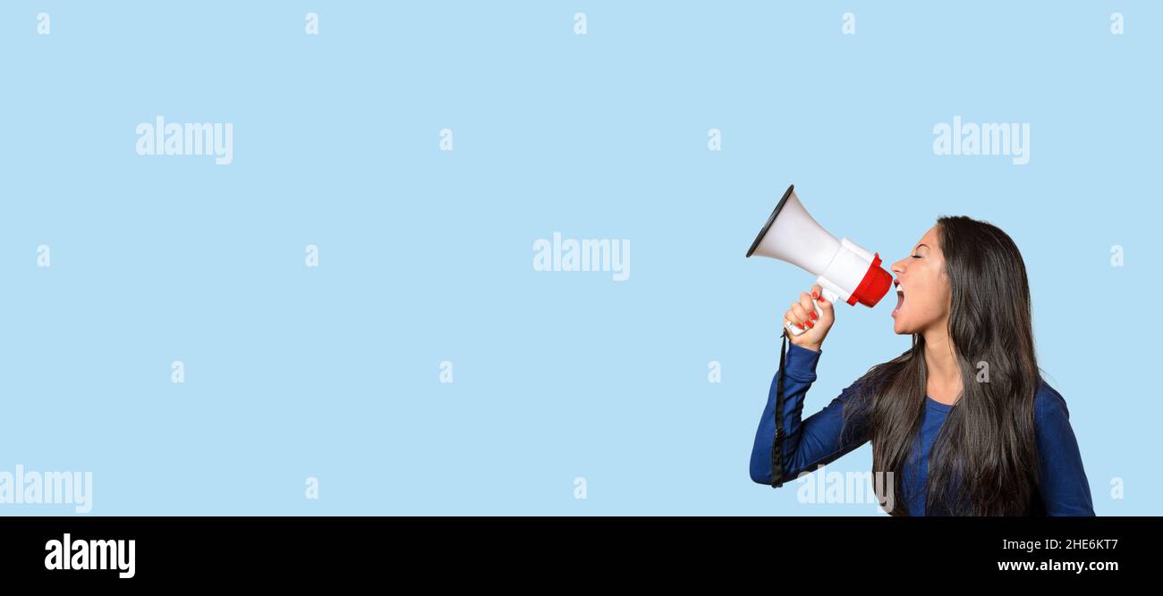 Young woman yelling over a loud hailer or megaphone in a conceptual image on blue with copyspace Stock Photo