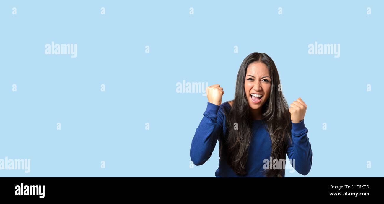 Enthusiastic young woman throwing a temper tantrum balling her fists and yelling at the camera over blue with copyspace Stock Photo