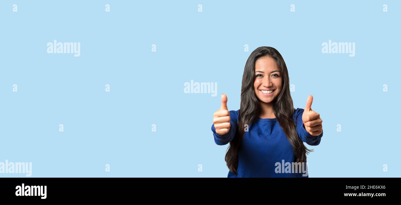 Elated successful young woman giving a double thumbs up with a beaming smile over blue with copyspace Stock Photo