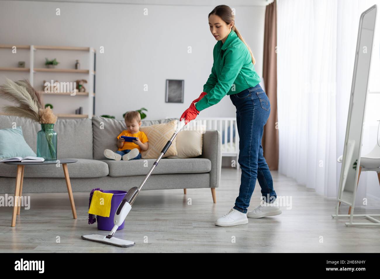Young mother cleaning house, mopping the floor and tidying up while