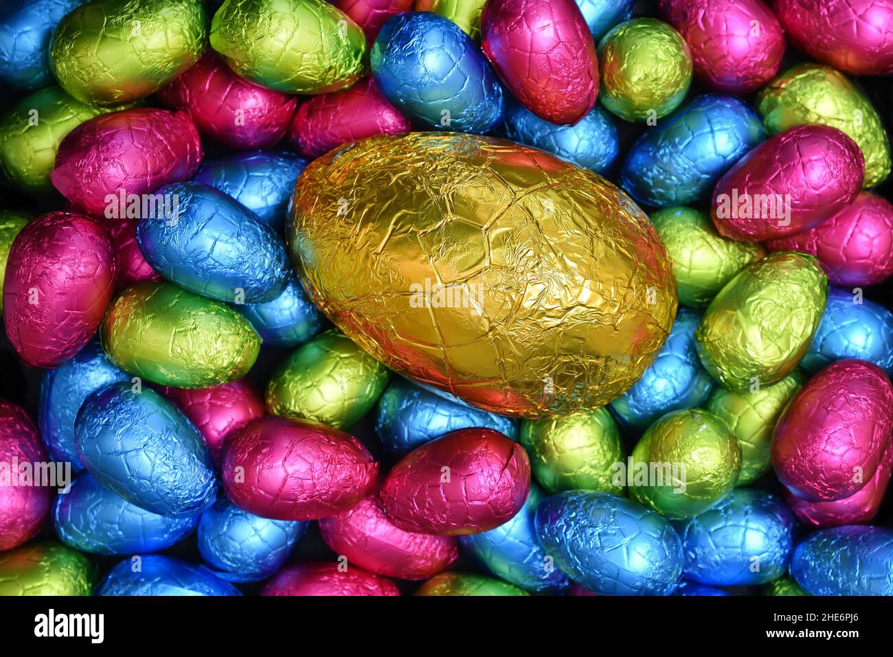 Pile or group of multi coloured and different sizes of colourful foil wrapped chocolate easter eggs in pink, blue, yellow and lime green. Stock Photo