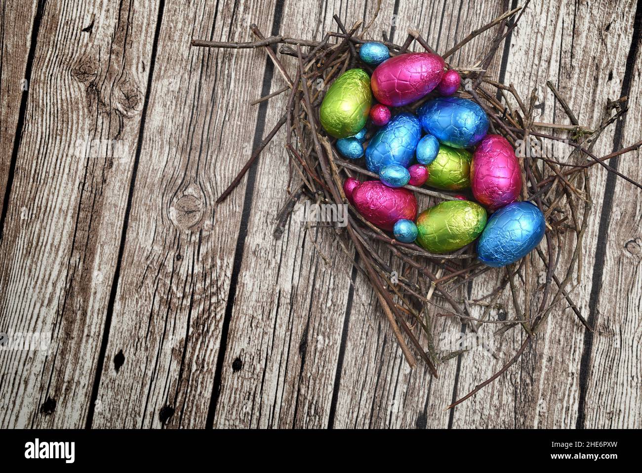 Foil wrapped colourful easter eggs in pink, green, blue and yellow in a natural nest made of sticks and twigs, against a multi grain brown background. Stock Photo