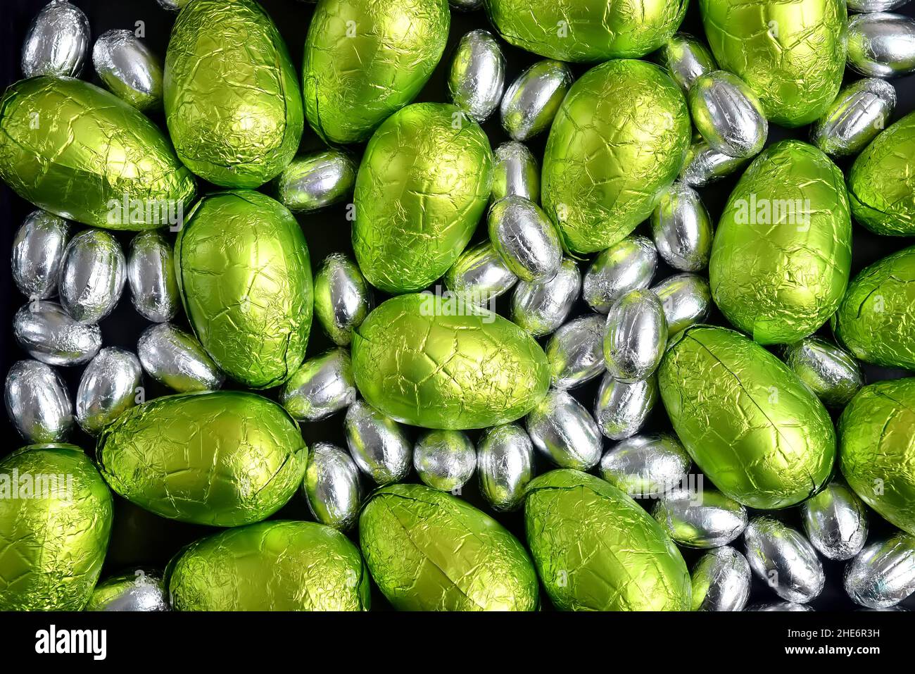 Large & small green, lime green and silver spring colours of foil wrapped chocolate easter eggs, against a black background. Stock Photo