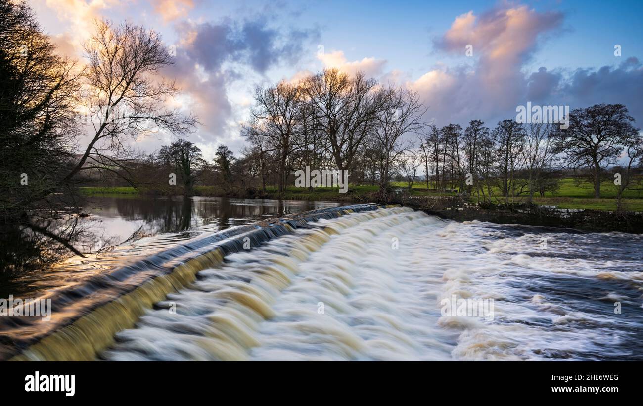 Scenic beautiful colourful sky & rural landscape (water flow pouring down weir steps) - River Wharfe, Burley in Wharfedale, Yorkshire, England, UK. Stock Photo