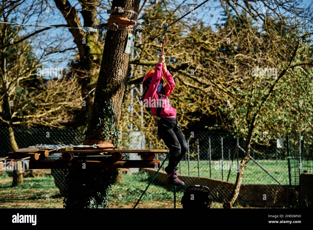 Little girl with protections practicing climbing between trees with ropes and nets Stock Photo