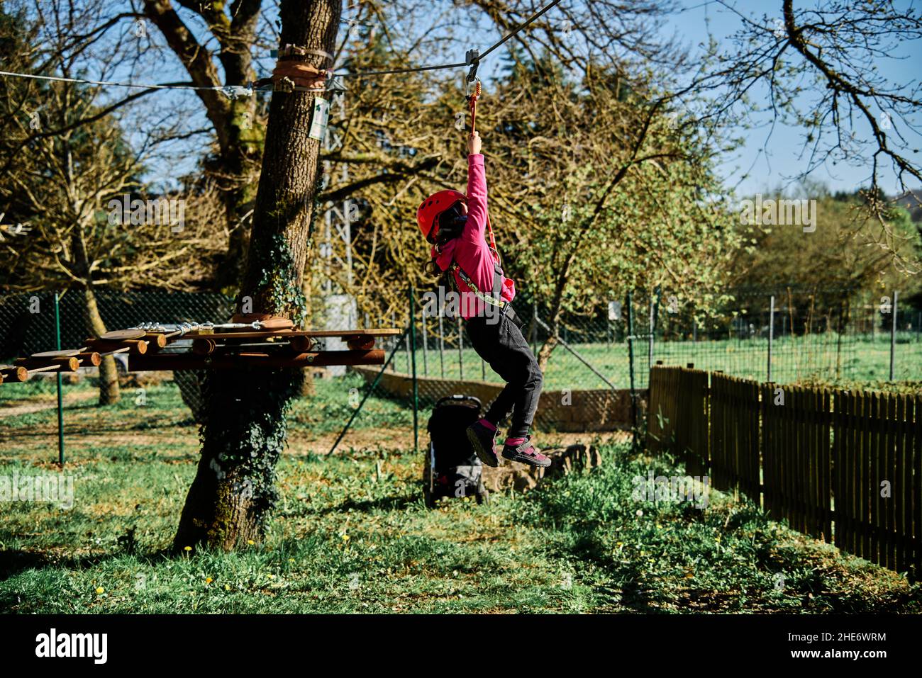 Little girl with protections practicing climbing between trees with ropes and nets Stock Photo