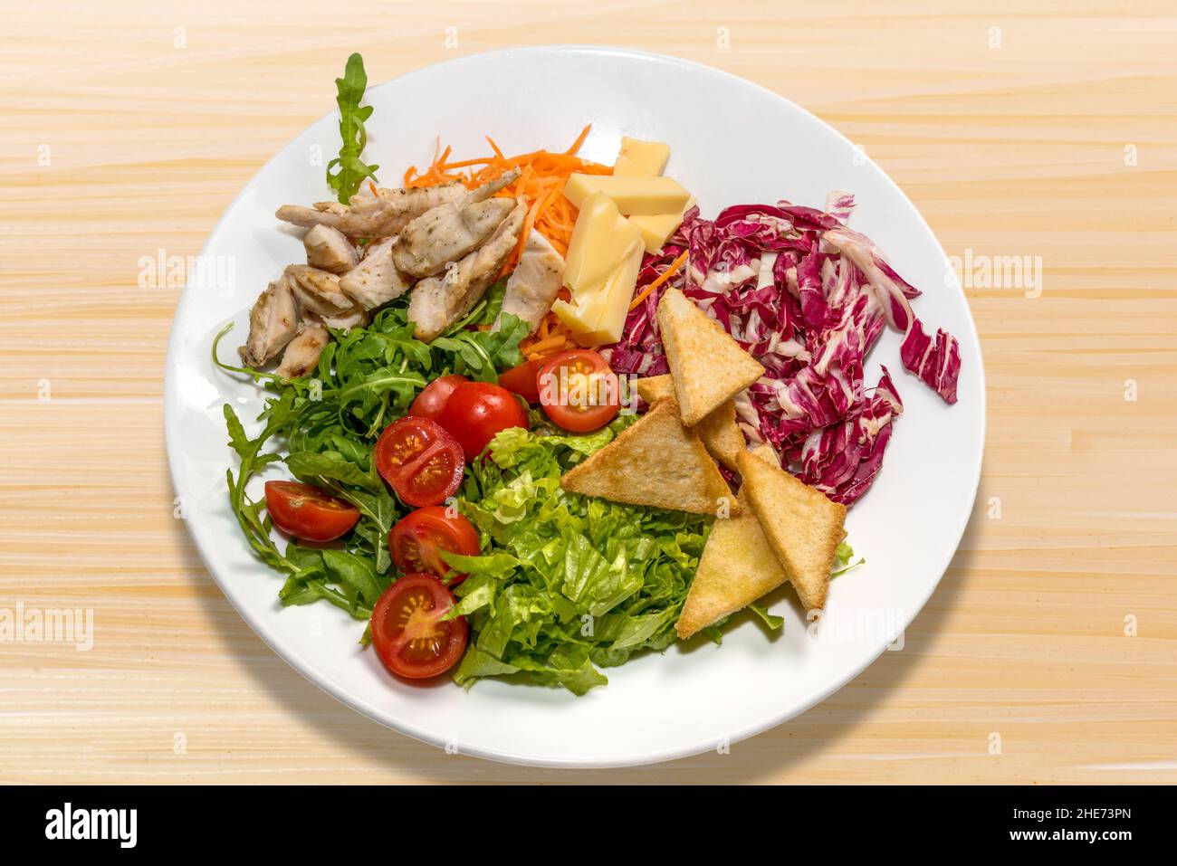 Caesar salad with chicken, cheese, tomato and croutons in white plate on wooden background Stock Photo