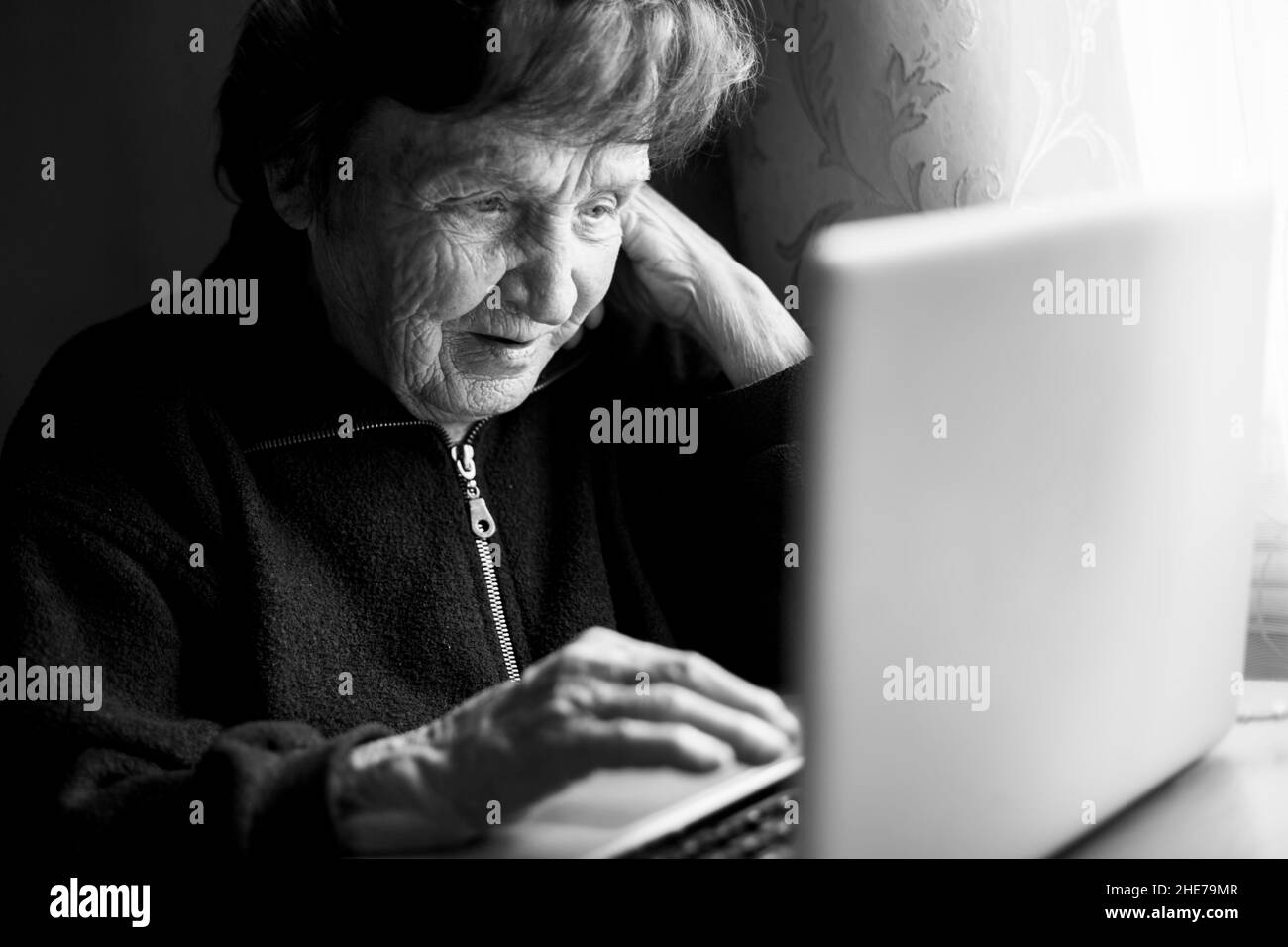 Old woman working on the computer in her home. Black and white photo. Stock Photo