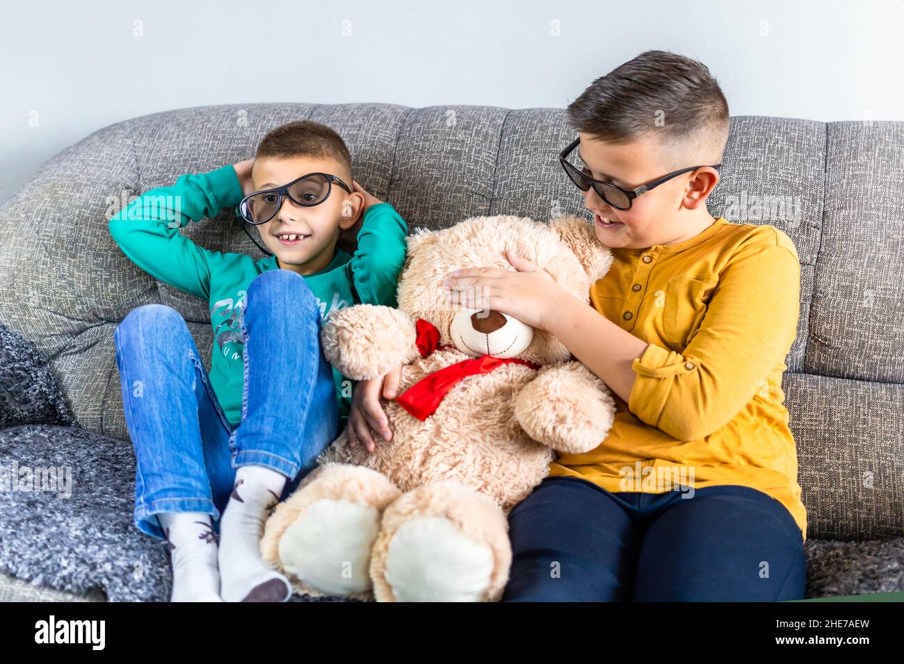 Cute boys, bothers watching movie with 3d glasses, sitting on the sofa in living room, together with teddy bear toy Stock Photo