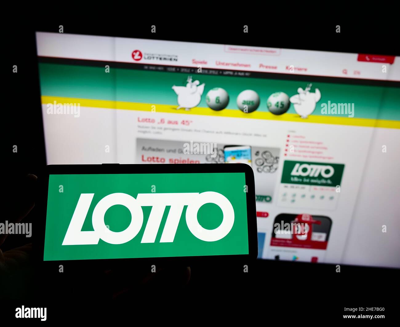 Person holding smartphone with logo of Austrian lottery of Österreichische Lotterien GmbH on screen in front of website. Focus on phone display. Stock Photo