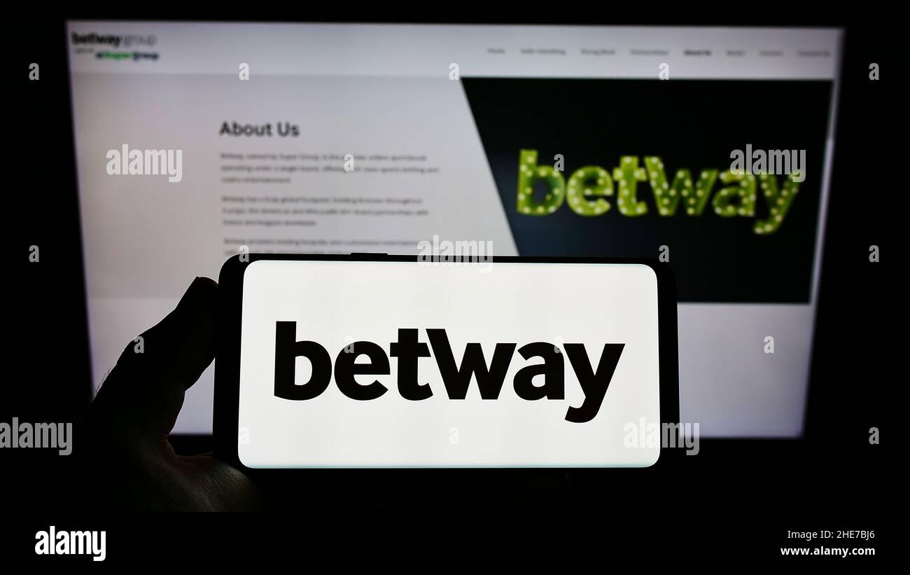 Person holding smartphone with logo of sports betting company Betway Group on screen in front of website. Focus on phone display. Stock Photo