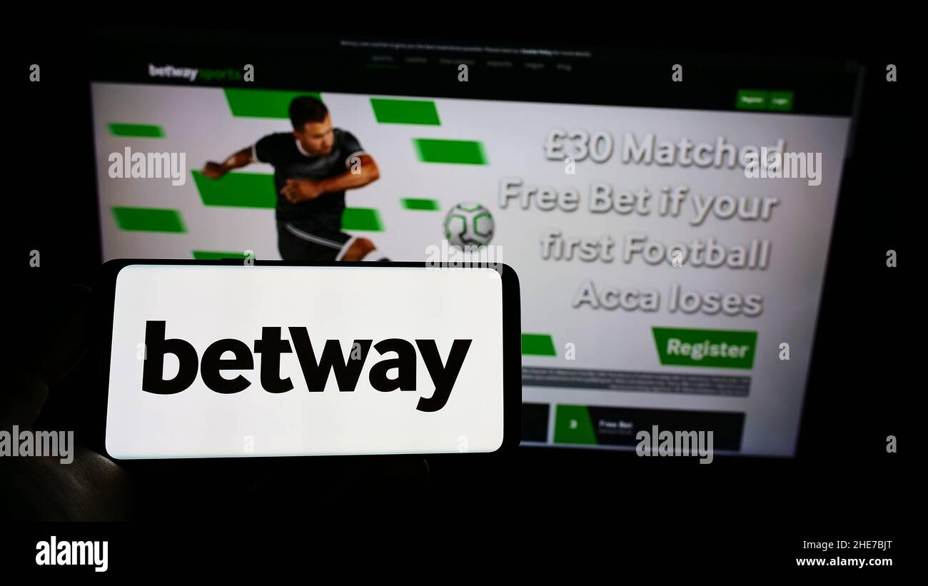 Person holding mobile phone with logo of sports betting company Betway Group on screen in front of business web page. Focus on phone display. Stock Photo