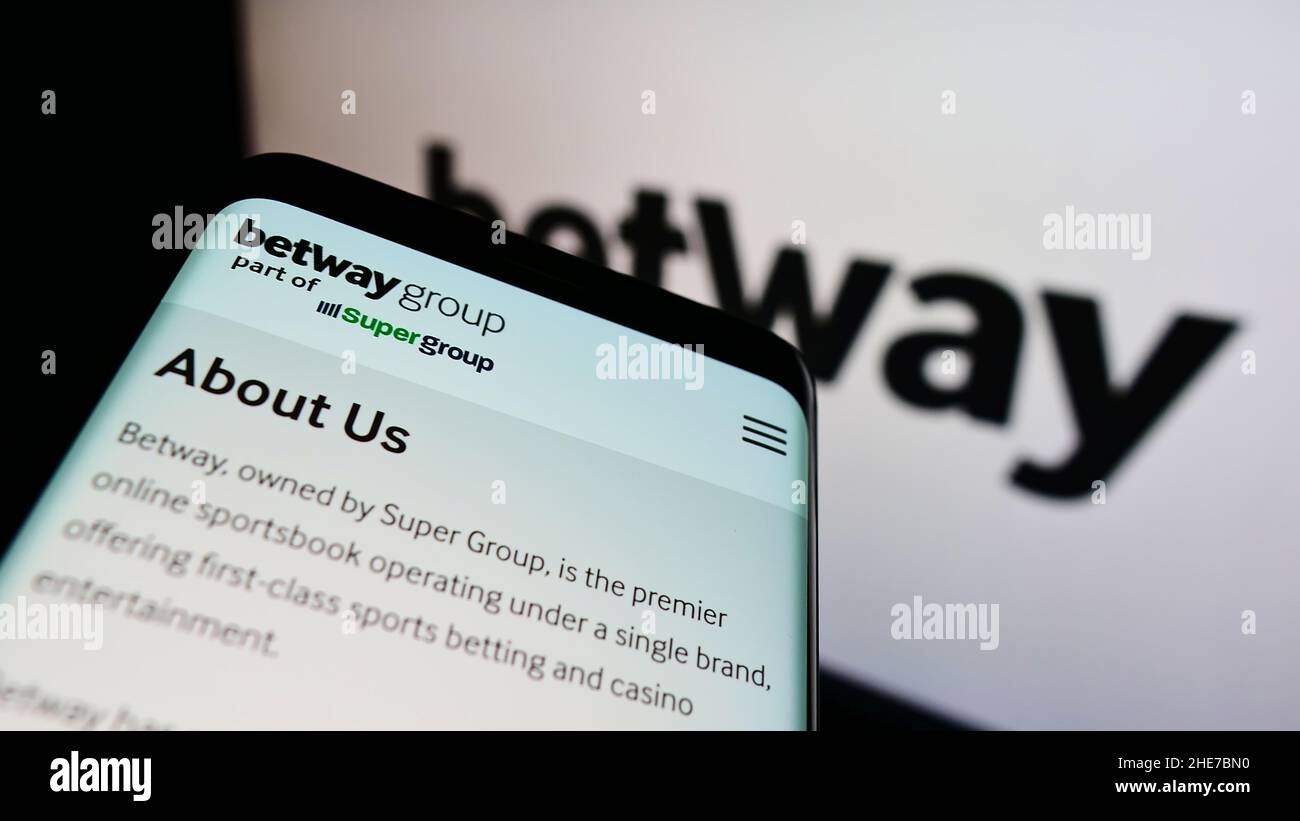 Mobile phone with webpage of sports betting company Betway Group on screen in front of business logo. Focus on top-left of phone display. Stock Photo