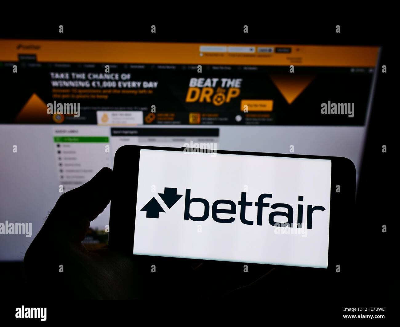 Person holding smartphone with logo of British online gambling company Betfair on screen in front of website. Focus on phone display. Stock Photo
