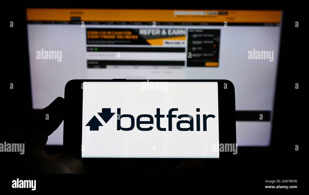 Person holding cellphone with logo of British online gambling company Betfair on screen in front of business webpage. Focus on phone display. Stock Photo
