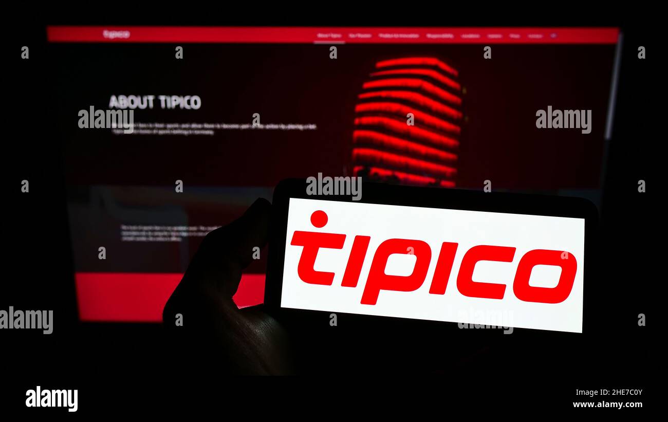 Person holding smartphone with logo of sports betting company Tipico Co. Ltd on screen in front of website. Focus on phone display. Stock Photo