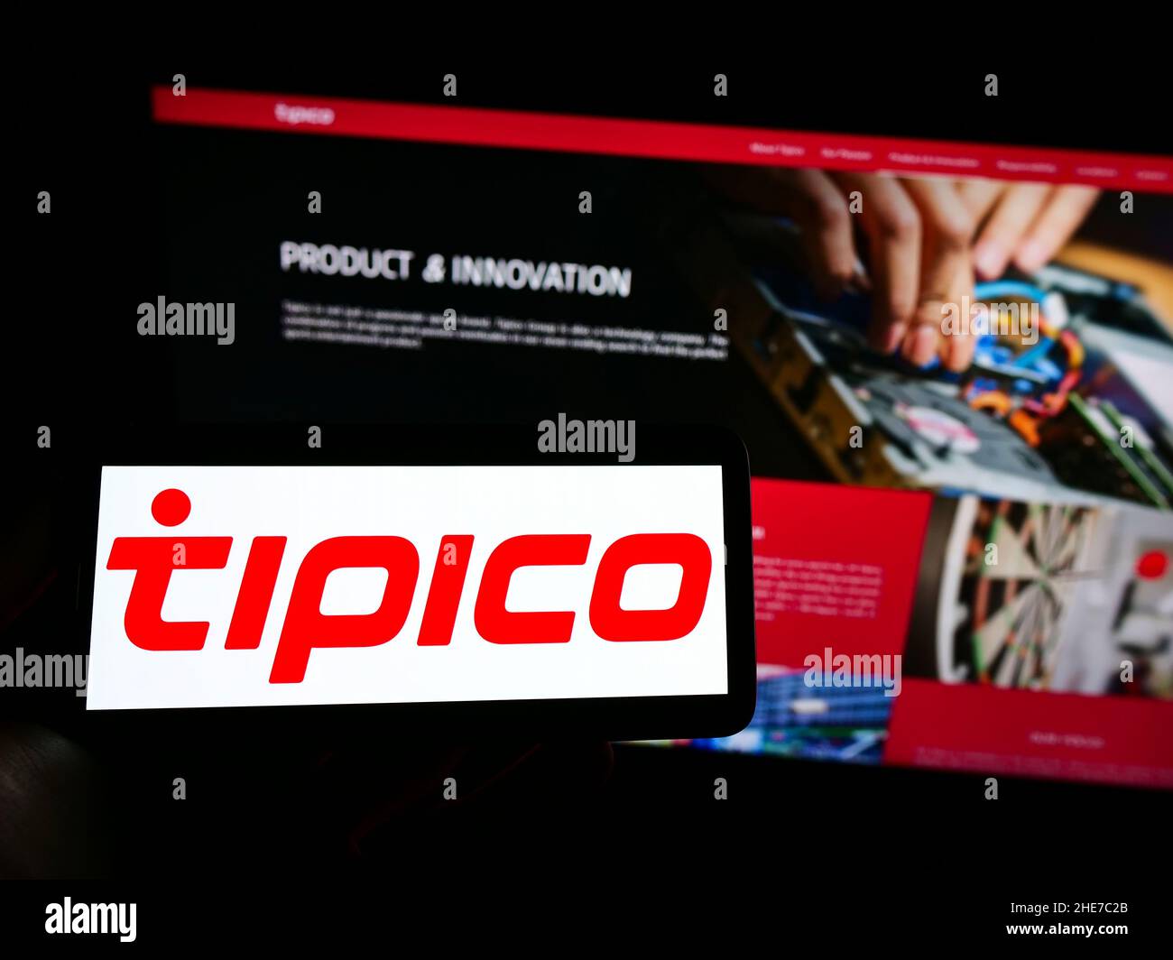 Person holding mobile phone with logo of sports betting company Tipico Co. Ltd on screen in front of business web page. Focus on phone display. Stock Photo