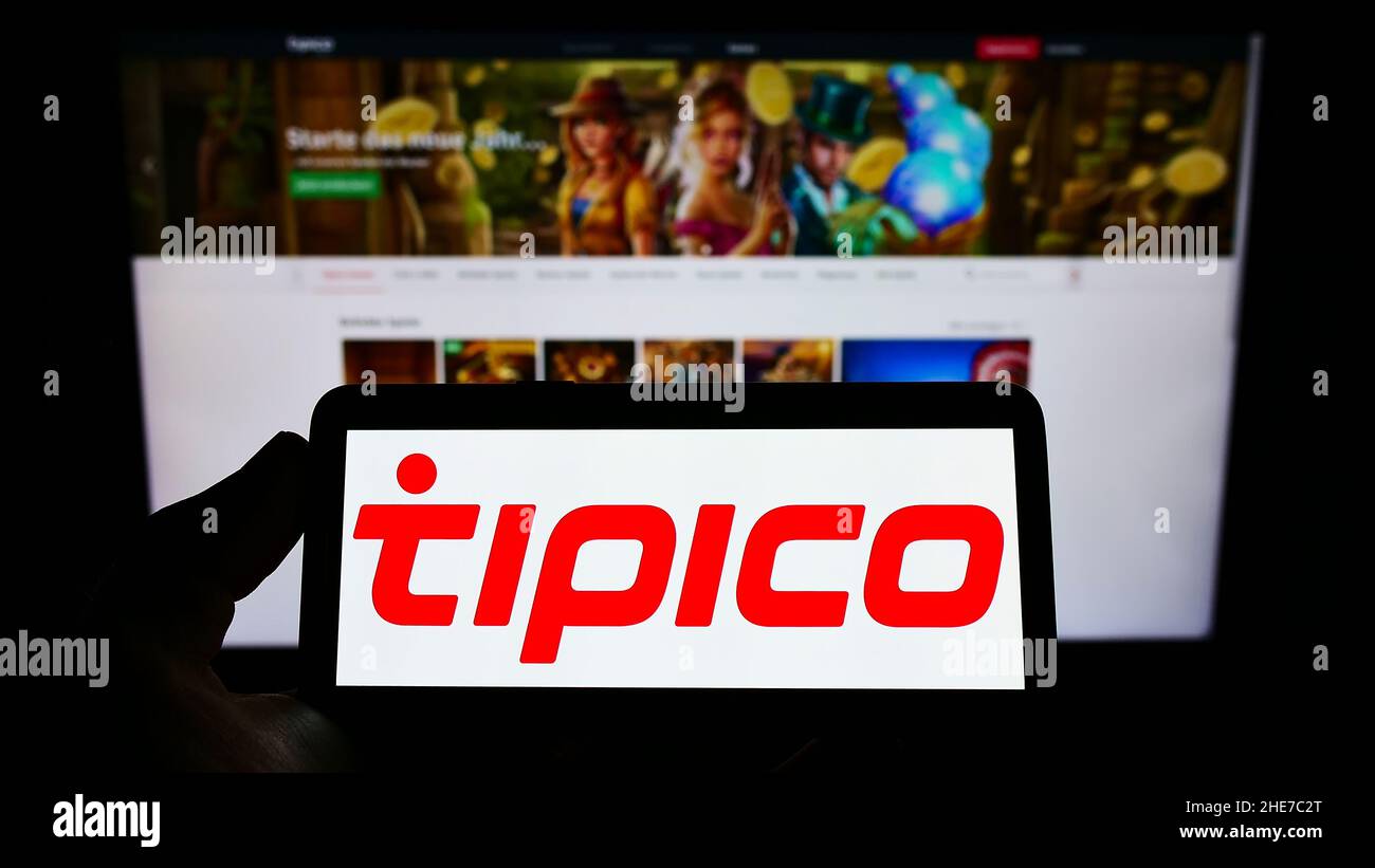 Person holding cellphone with logo of sports betting company Tipico Co. Ltd on screen in front of business webpage. Focus on phone display. Stock Photo