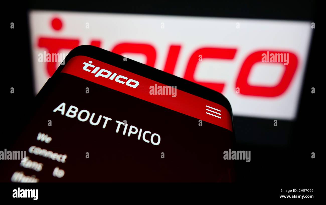 Mobile phone with webpage of sports betting company Tipico Co. Ltd on screen in front of business logo. Focus on top-left of phone display. Stock Photo