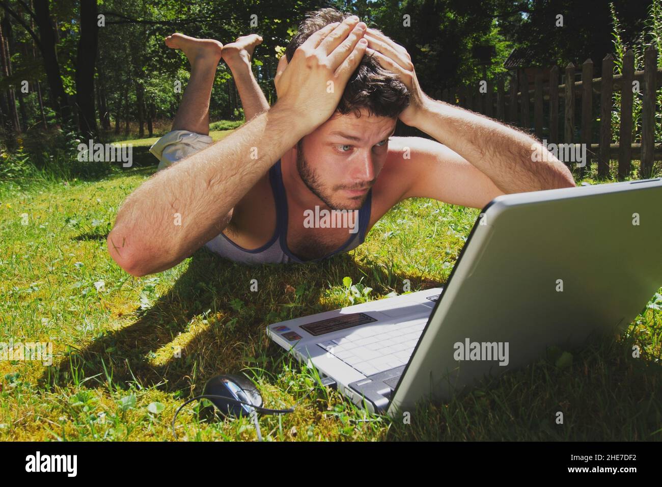Junger Mann auf dem Rasen mit Laptop | young man lying on lawn and working with a laptop Stock Photo