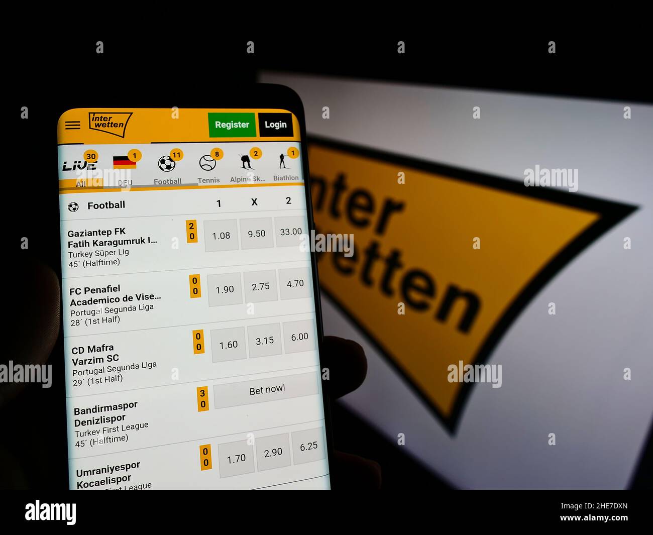 Person holding cellphone with website of sports betting company Interwetten Ltd. on screen in front of logo. Focus on center of phone display. Stock Photo