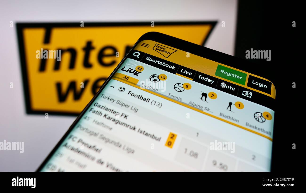 Mobile phone with webpage of sports betting company Interwetten Ltd. on screen in front of business logo. Focus on top-left of phone display. Stock Photo