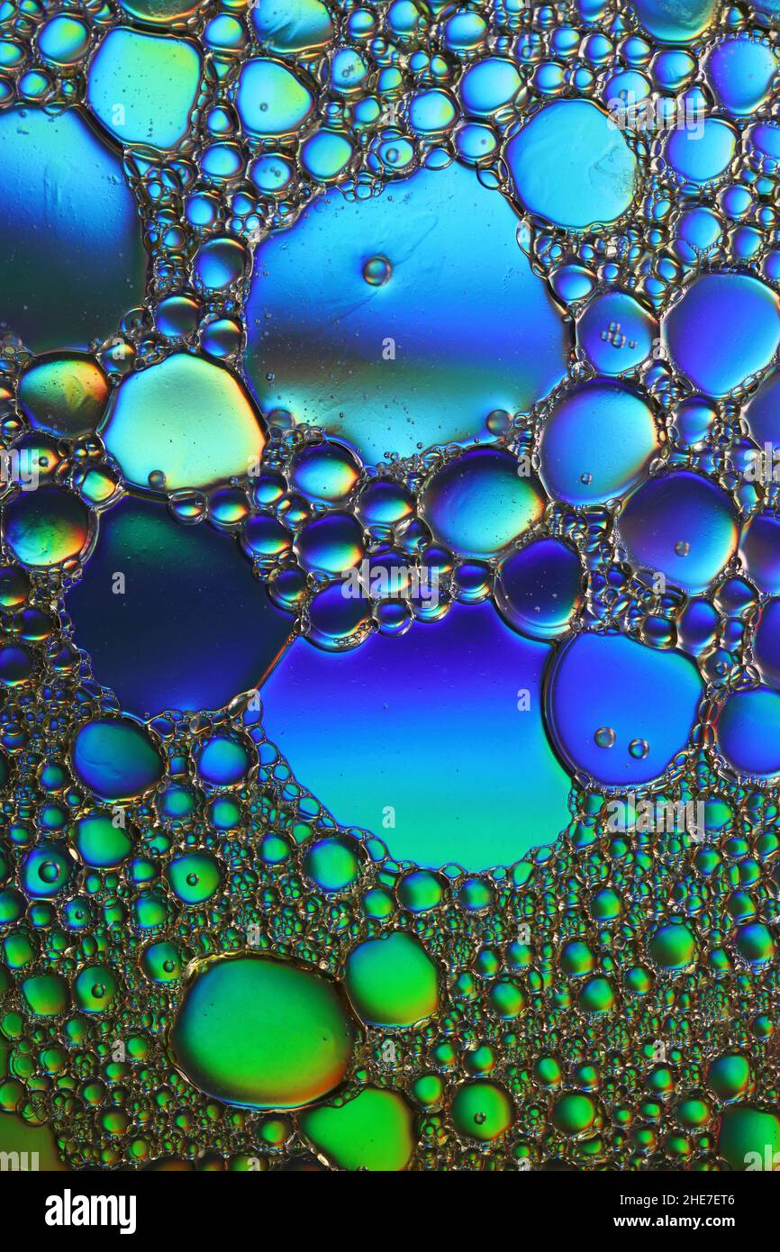 green and blue illuminated oil droplets float on a water surface, macro