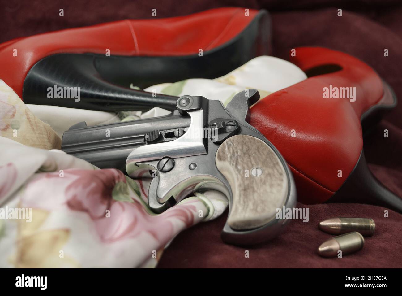 The end of an affair. A handgun, bullets, red high heels and nightie on dark red velvet. Stock Photo