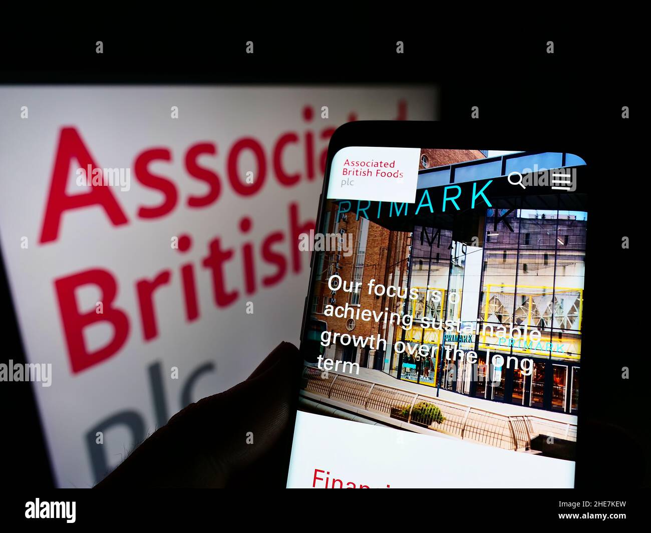 Person holding smartphone with webpage of company Associated British Foods plc (ABF) on screen in front of logo. Focus on center of phone display. Stock Photo