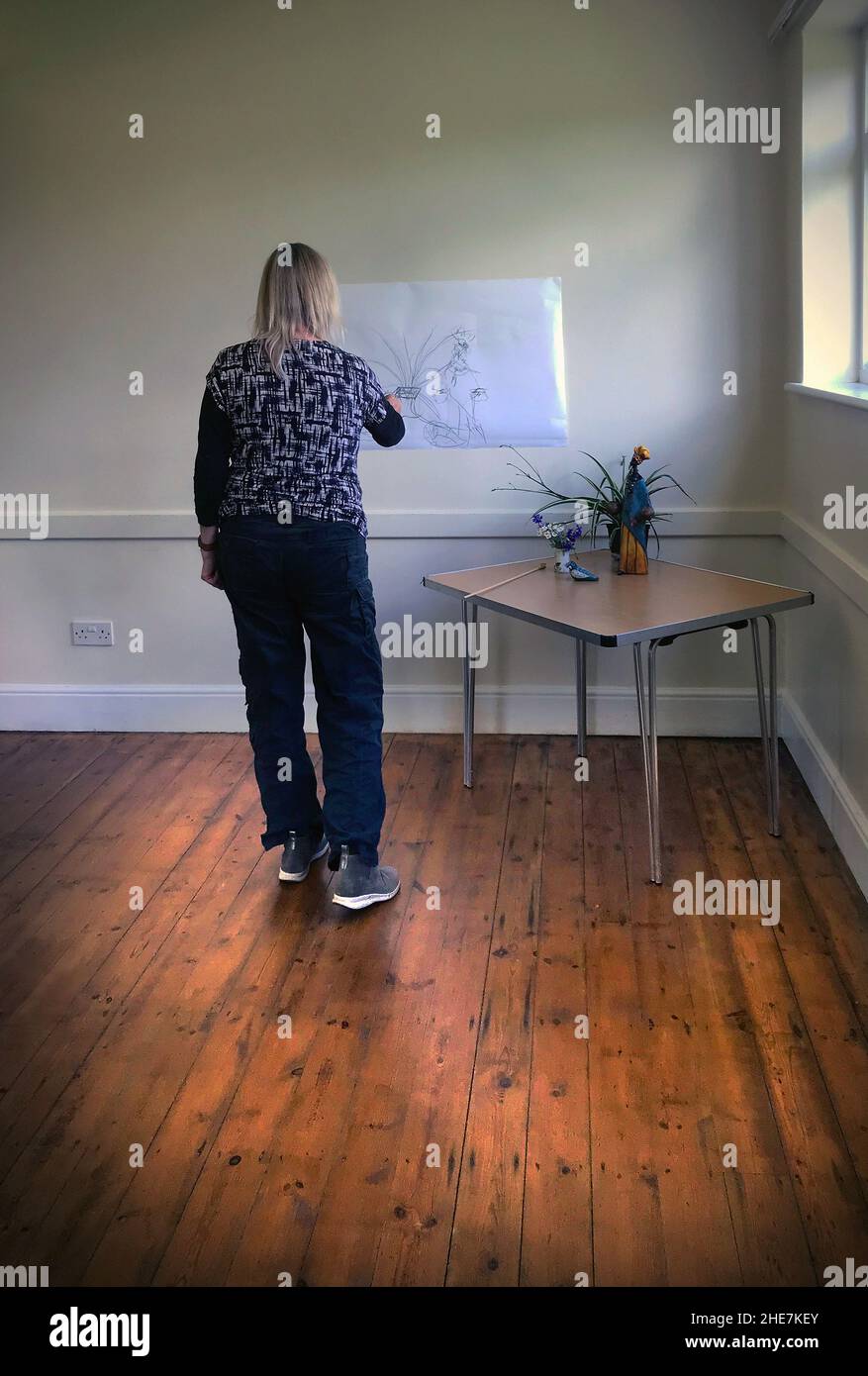 solitary woman drawing on paper attached to wall Stock Photo