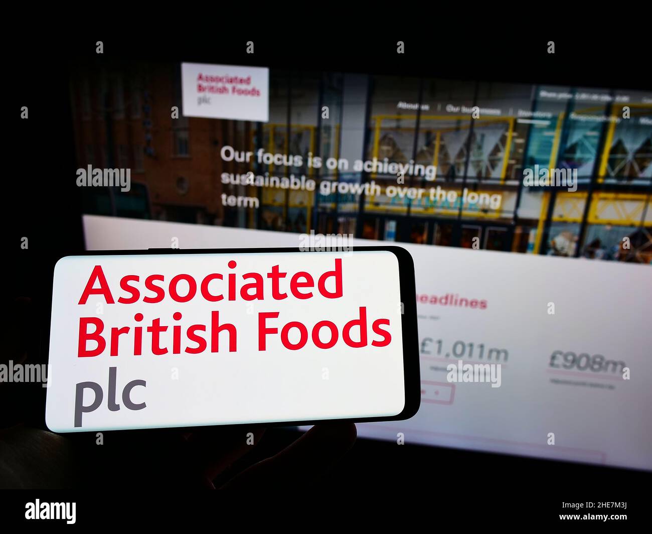 Person holding cellphone with logo of company Associated British Foods plc (ABF) on screen in front of business web page. Focus on phone display. Stock Photo
