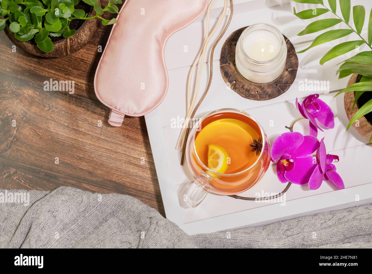 Insomnia or depression treatment. Home relaxing concept. Wooden tray with cup of fruit tea with lemon slice, aroma candle and sticks with palm leaves Stock Photo