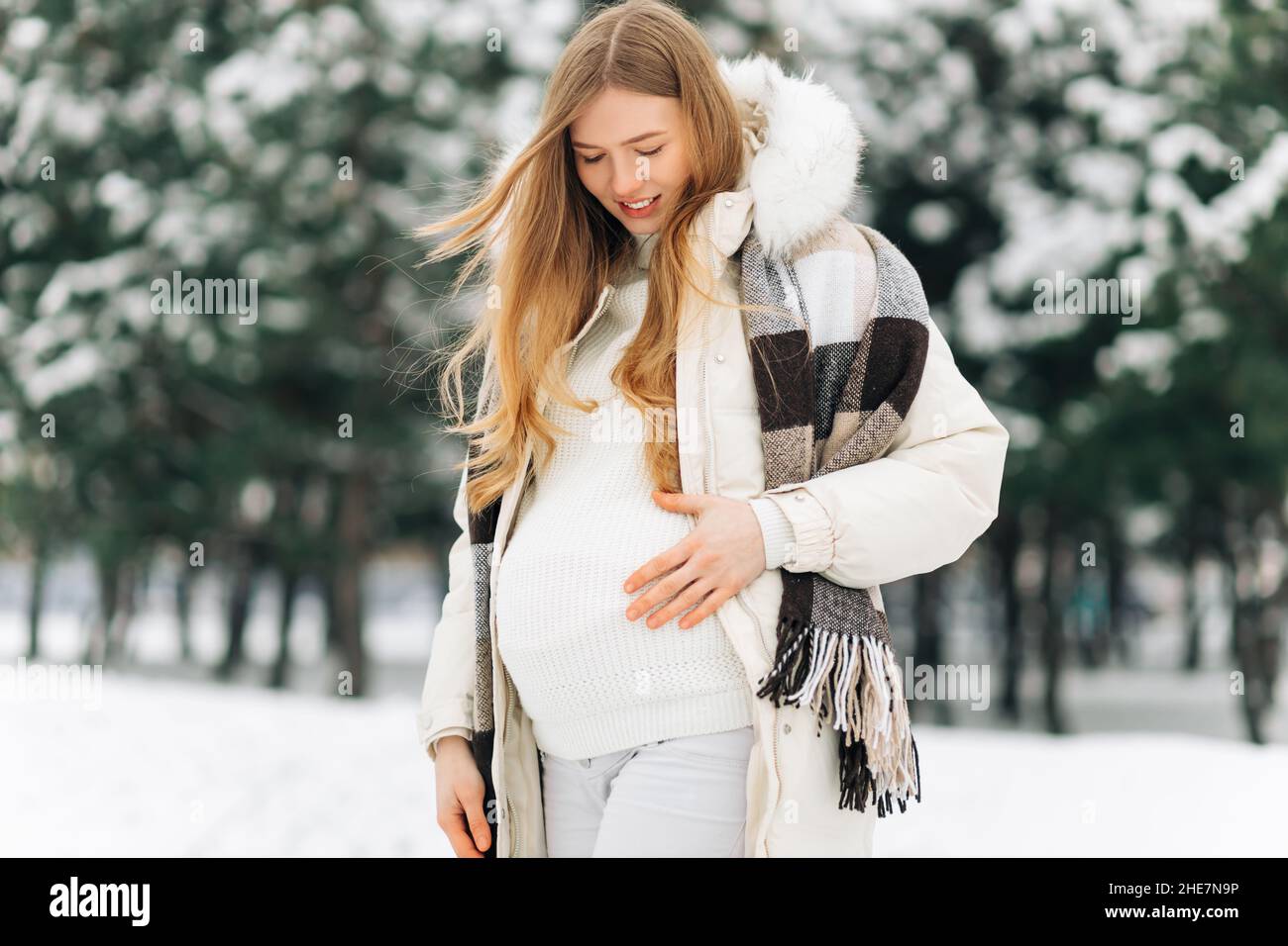 pregnant woman in warm winter clothes standing outside on a snowy winter  day, with hands on her stomach on the background of nature. Concept of  pregna Stock Photo - Alamy