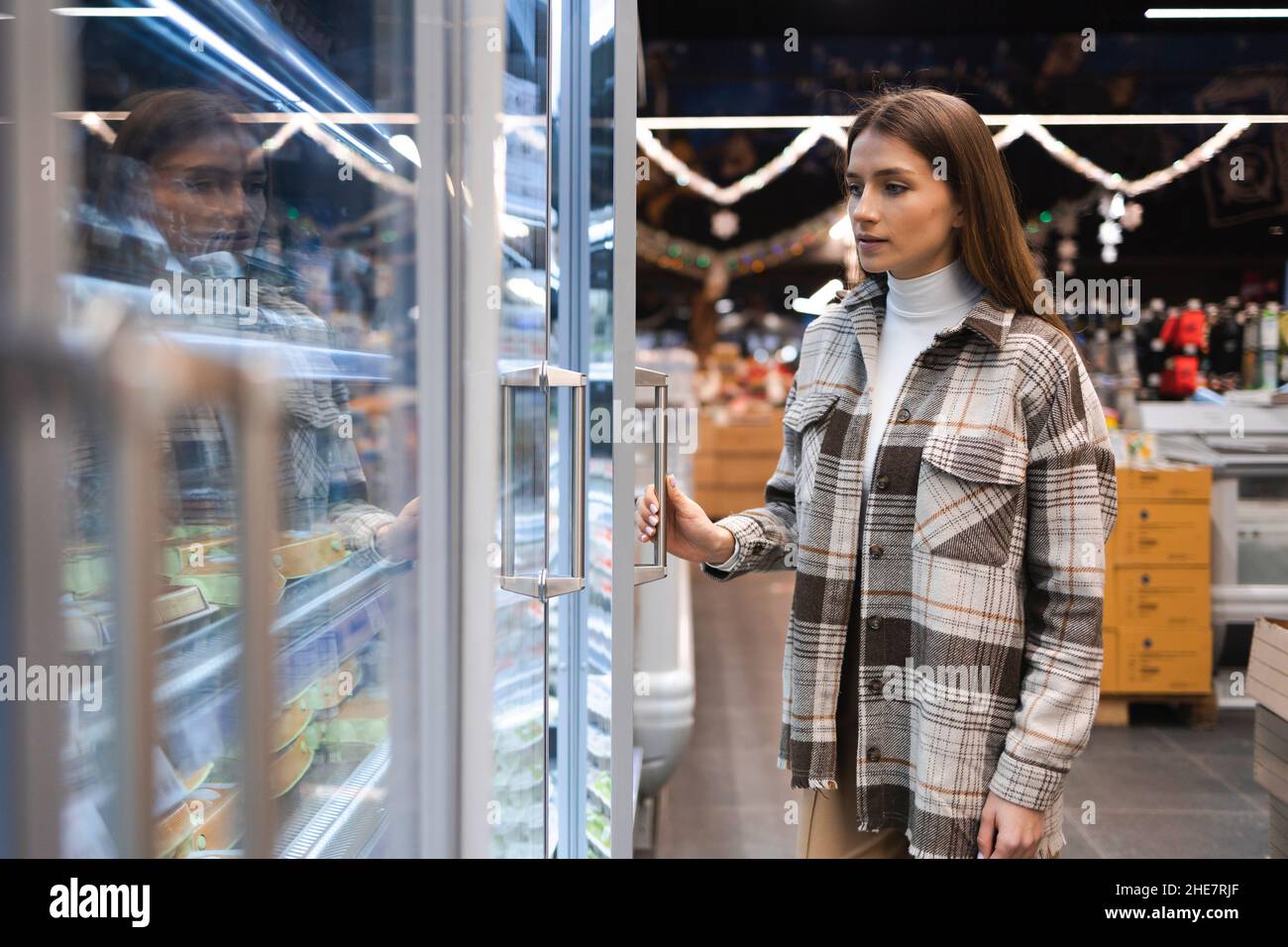Woman opens the refrigerator door with a product in a supermarket. Girl chooses eggs in the grocery store Stock Photo
