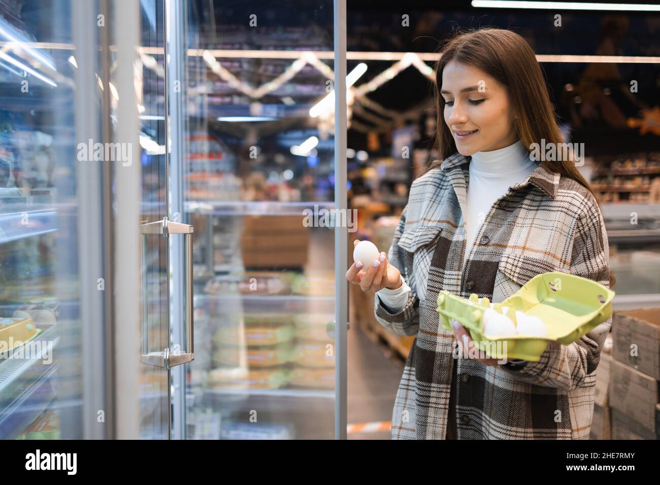 Pretty young woman buys chicken eggs in supermarket. Girl chooses products in a grocery store Stock Photo